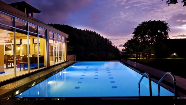 A modern hotel with a swimming pool, large windows, and a view of a forested area. - Melheim Kandy Villas (Kandy)