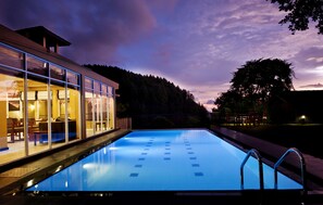 A modern hotel with a swimming pool, large windows, and a view of a forested area.