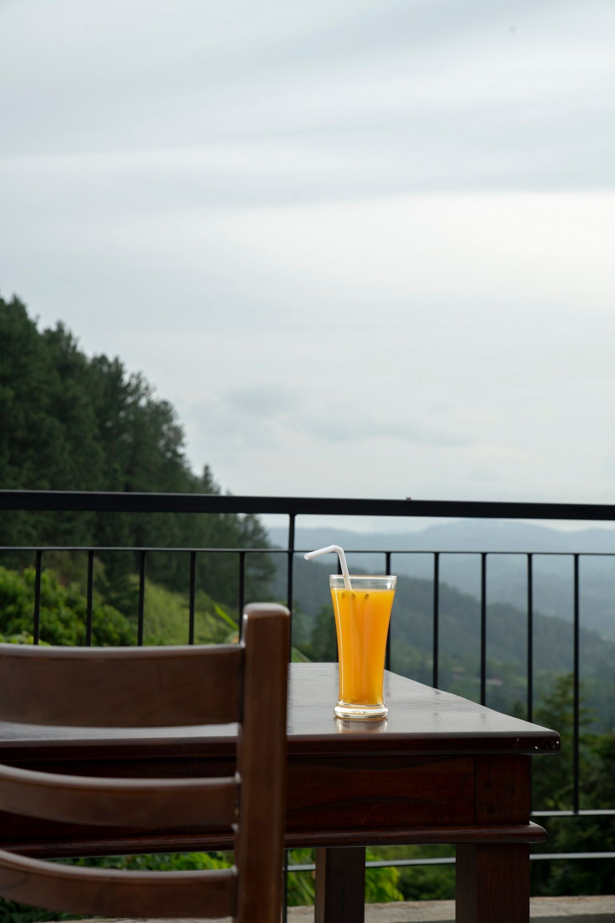 Een tafel met een glas sinaasappelsap en een stoel, met uitzicht op een bergachtig landschap.