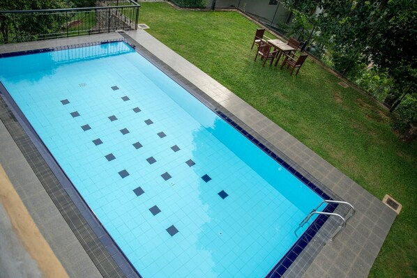 A rectangular swimming pool with a tiled deck and a grassy area with a table and chairs.