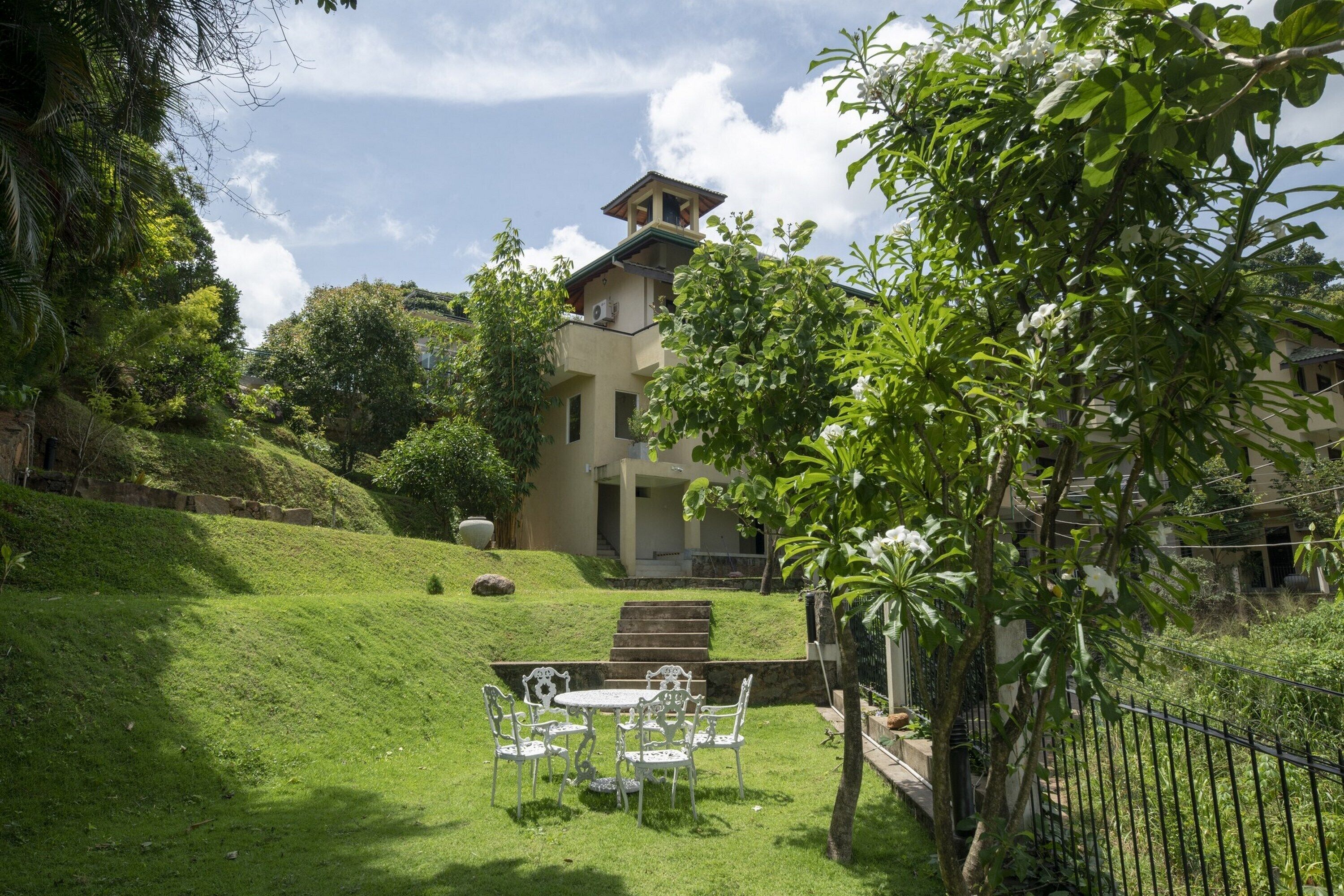 A building with a balcony, surrounded by lush greenery and a well-maintained lawn.