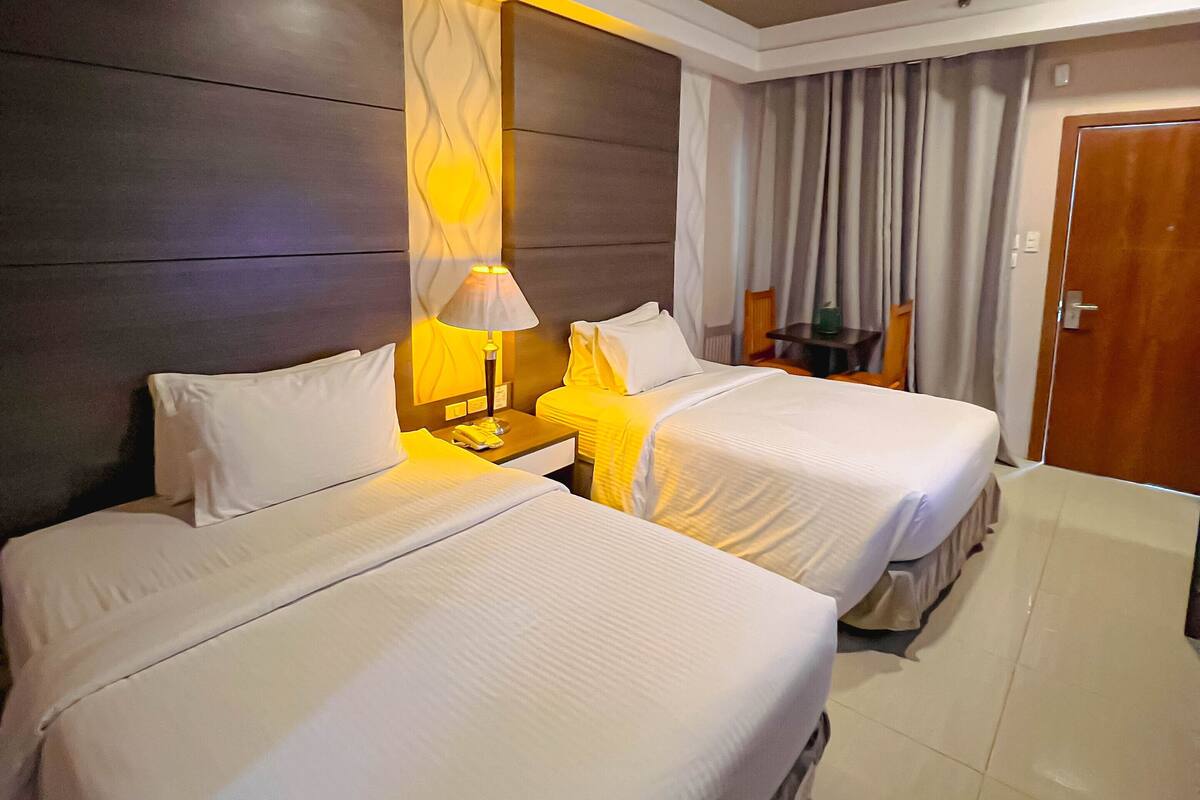 A hotel room with two beds, a nightstand with a lamp, a wooden headboard, and a door.