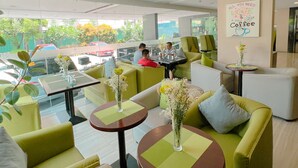 A modern lounge area with green sofas, round tables, and a large window offering a view of the outside. - 88 Courtyard Hotel (Pasay)