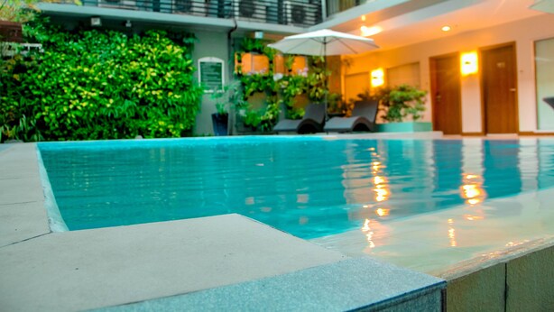 A swimming pool with a tiled edge, surrounded by greenery and a balcony with chairs. - 88 Courtyard Hotel (Pasay)