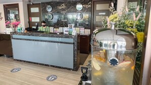 A hotel reception area with a marble counter, clocks indicating different cities, a large beverage dispenser, and a shuttle service sign. - 88 Courtyard Hotel (Pasay)