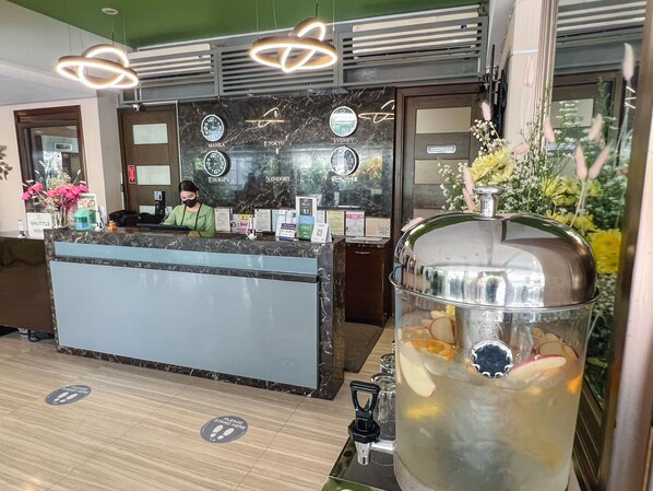 A hotel reception area with a marble counter, clocks indicating different cities, a large beverage dispenser, and a shuttle service sign. - 88 Courtyard Hotel (Pasay)