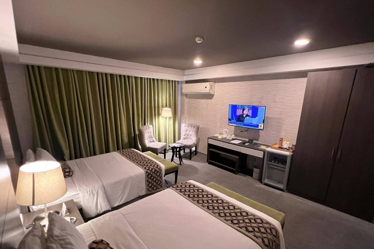 A hotel room with two beds, a desk, a TV, and a chair.