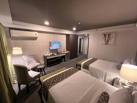 A hotel room with two beds, a desk with a TV, a chair, and a lamp.