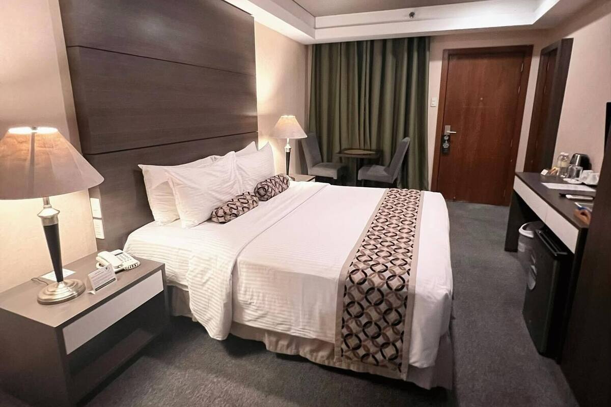 A hotel room with a large bed, bedside tables, a desk, and a chair.