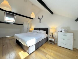 A bedroom with a bed, bedside tables, a dresser, a skylight, and a wall-mounted deer head decoration.