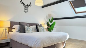 Une chambre à coucher moderne avec un grand lit, une décoration murale représentant une tête de cerf, un puits de lumière et une plante placée sur la table de chevet.