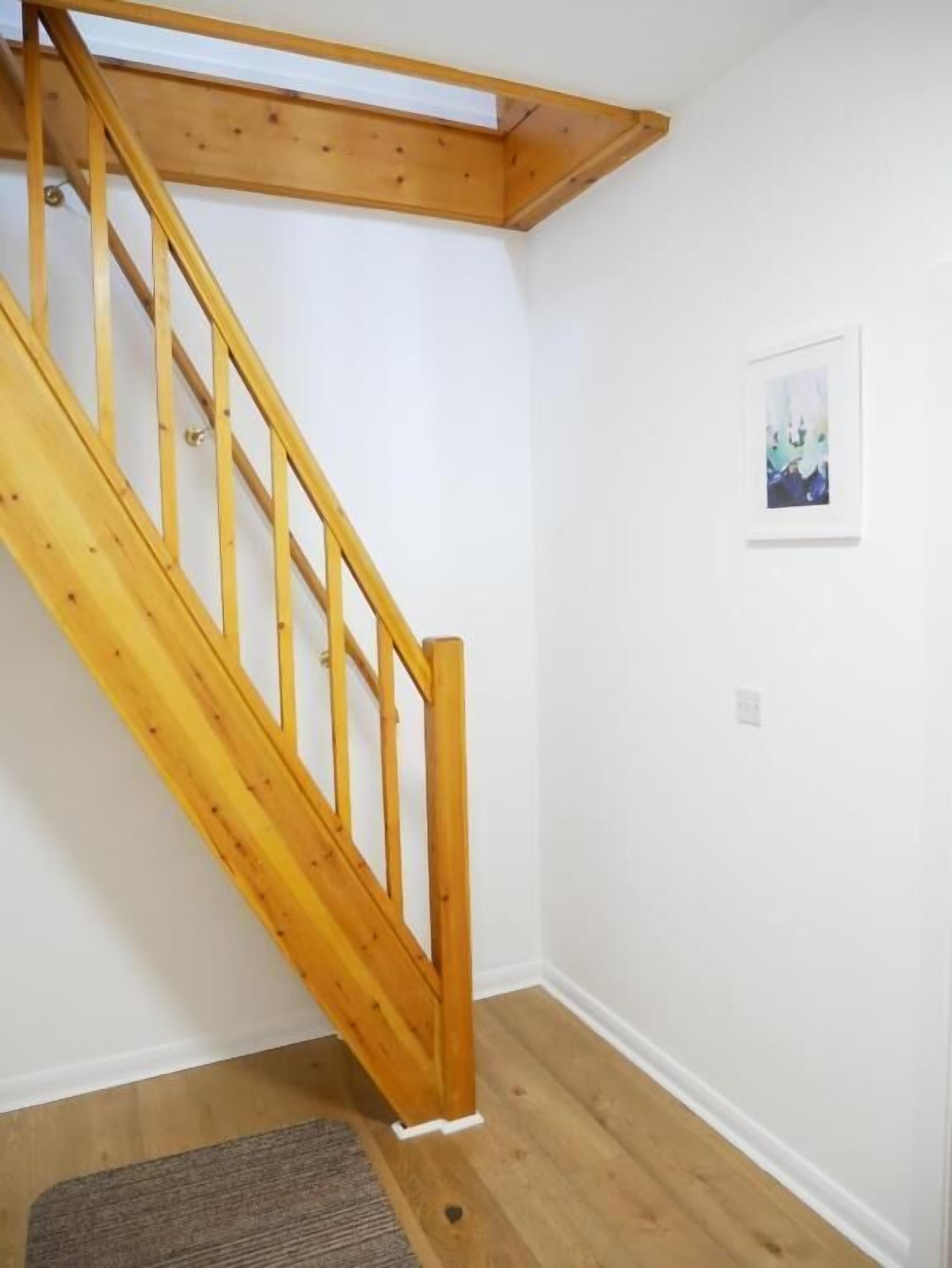 Eine Holztreppe mit Handlauf, einer weißen Wand und einem Bilderrahmen.