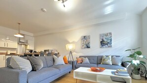 Un salon moderne avec un canapé gris, une table basse blanche et un coin repas, la cuisine étant visible au fond.