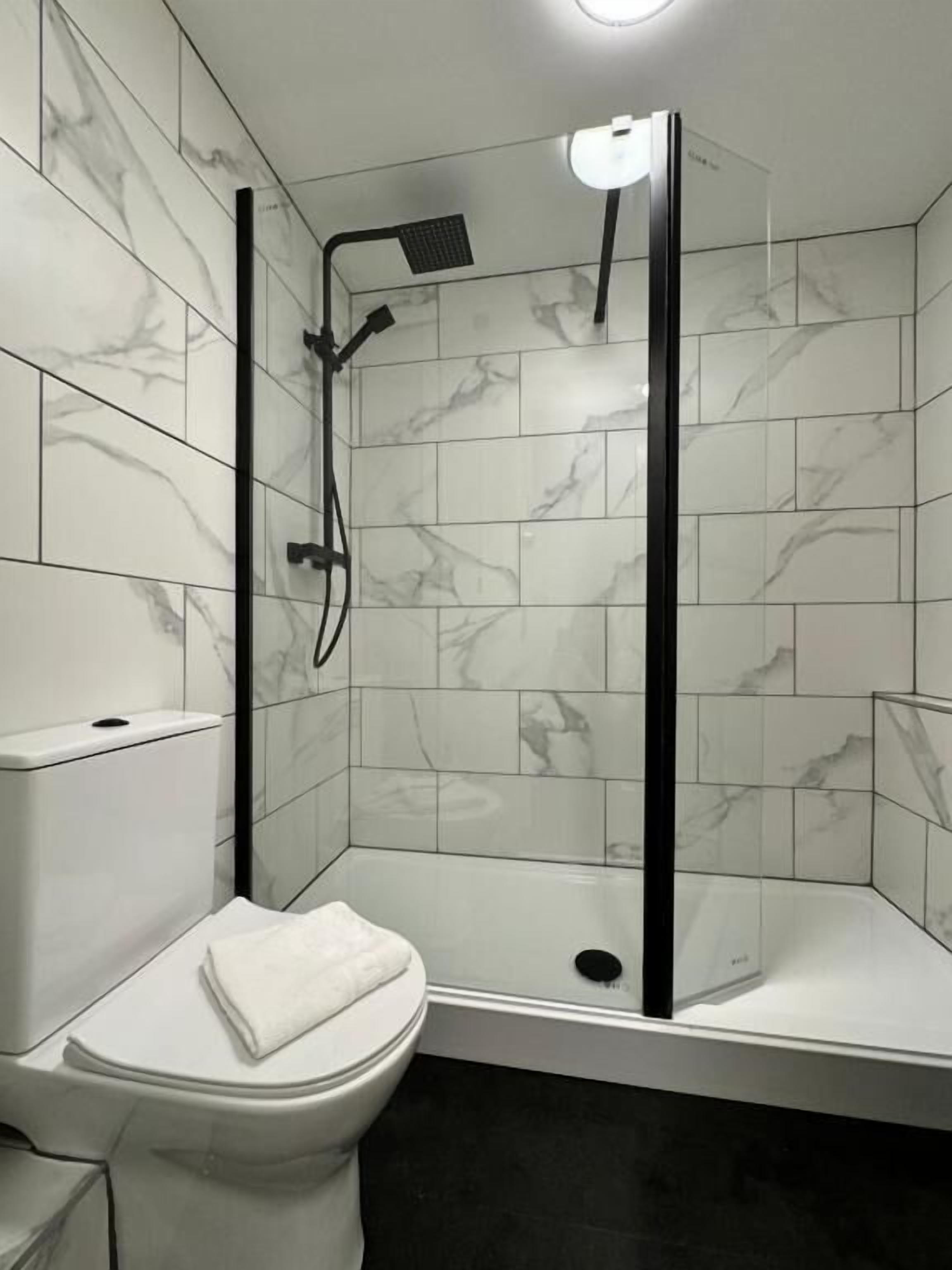 A bathroom with a toilet, a shower enclosure with a glass door, and a marble-tiled wall.