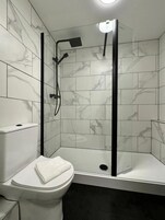 Un baño con inodoro, cabina de ducha con puerta de cristal y pared con azulejos de mármol.