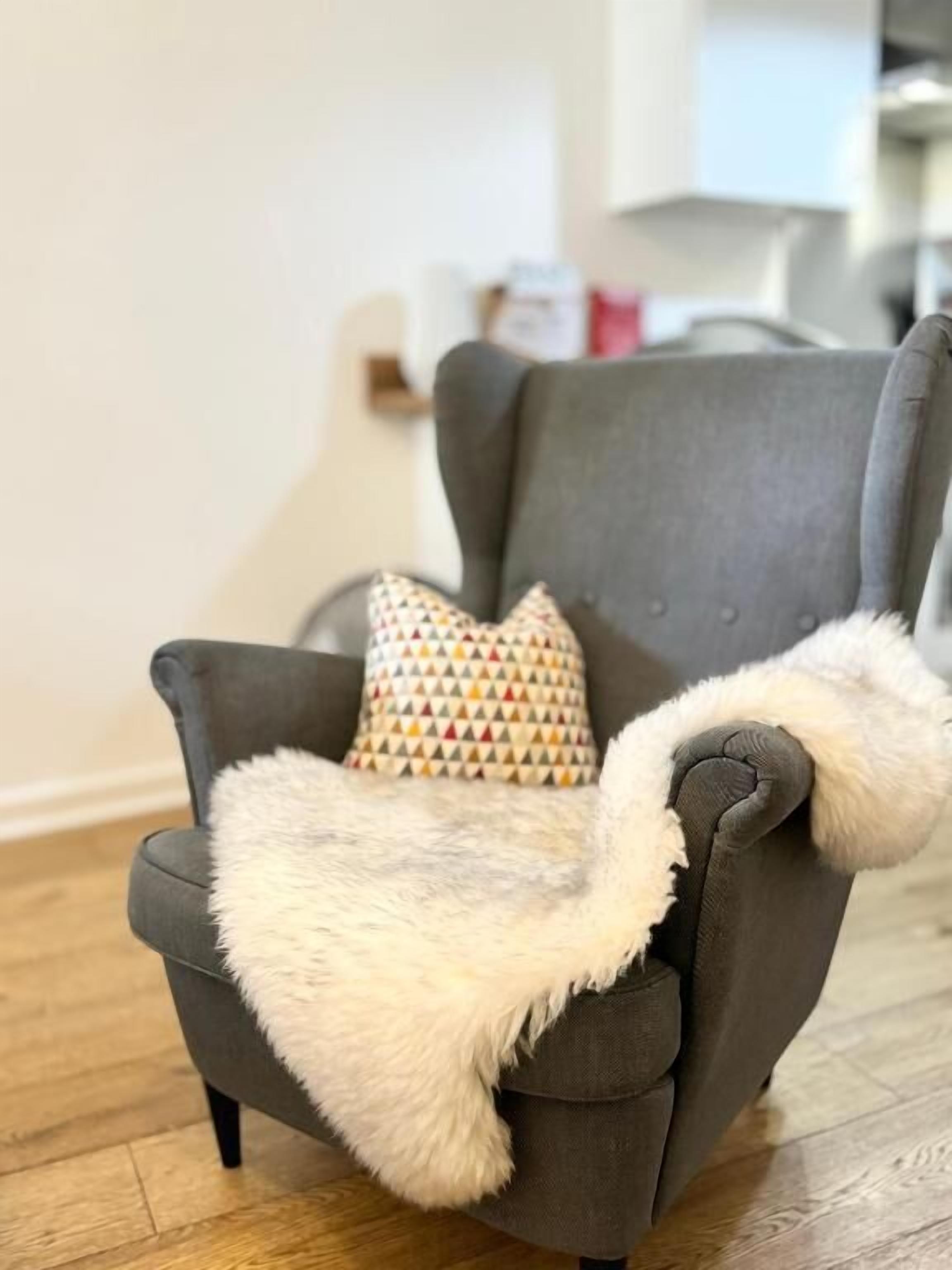 Un fauteuil gris avec un coussin à motifs et un plaid blanc et moelleux.