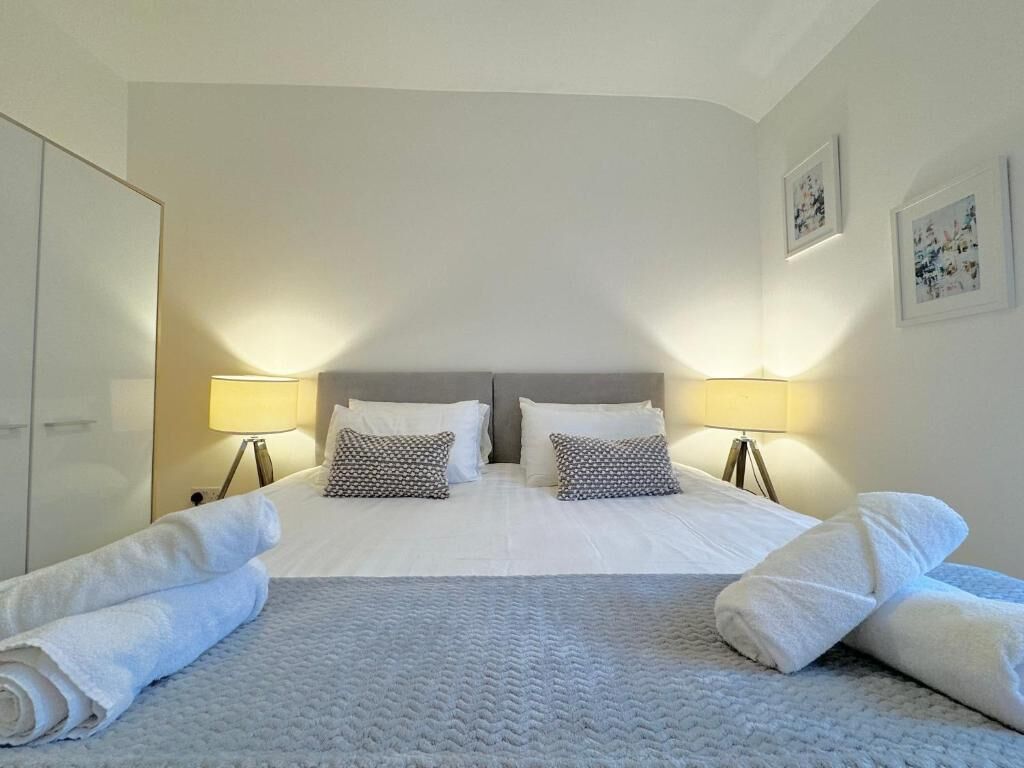 A hotel room with a large bed, two bedside lamps, a wardrobe, and a wall with framed pictures.