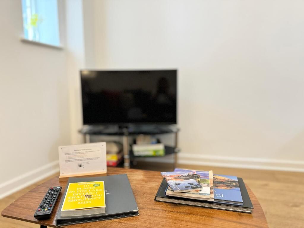 A room with a television on a stand, a remote control, a black binder, and a stack of brochures on a wooden table.