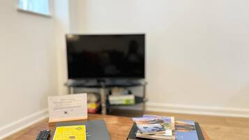 A room with a television on a stand, a remote control, a black binder, and a stack of brochures on a wooden table.