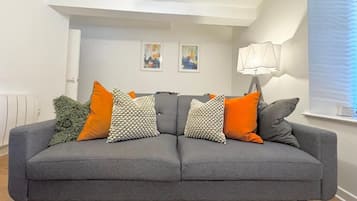 A grey sofa with multiple cushions, a wall-mounted lamp, and two framed artworks on the wall.