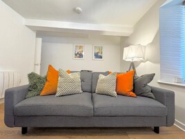 Un sofá gris con varios cojines, una lámpara de pared y dos cuadros en la pared.