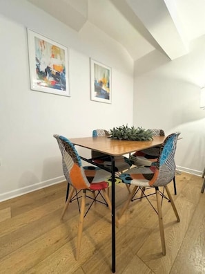 A dining area with a wooden table and two chairs with colorful patterns, a potted plant on the table, and two abstract paintings on the wall. - Nordic Suites (Ulverston)