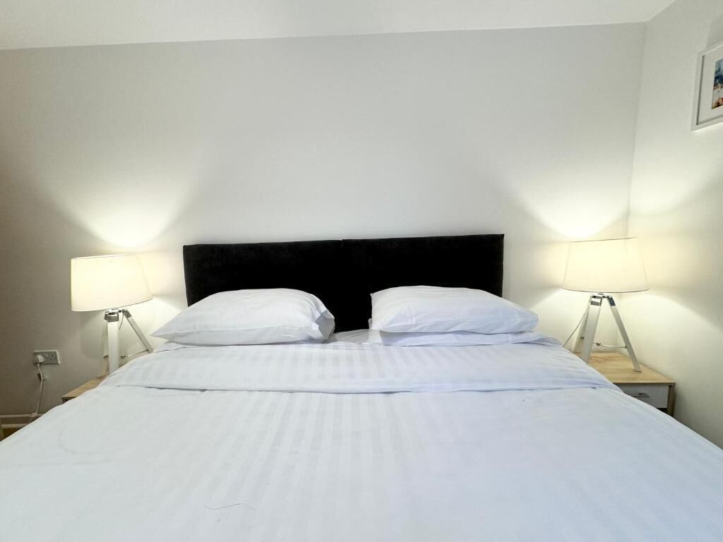 Un llit ben fet amb roba de llit blanca i un panell de capçal negre, amb dues làmpades de nit sobre taules de nit de fusta.