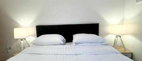 Un llit ben fet amb roba de llit blanca i un panell de capçal negre, amb dues làmpades de nit sobre taules de nit de fusta.