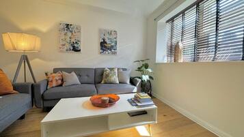 Una sala de estar con un sofá gris, una mesa de centro blanca y una lámpara de pie.