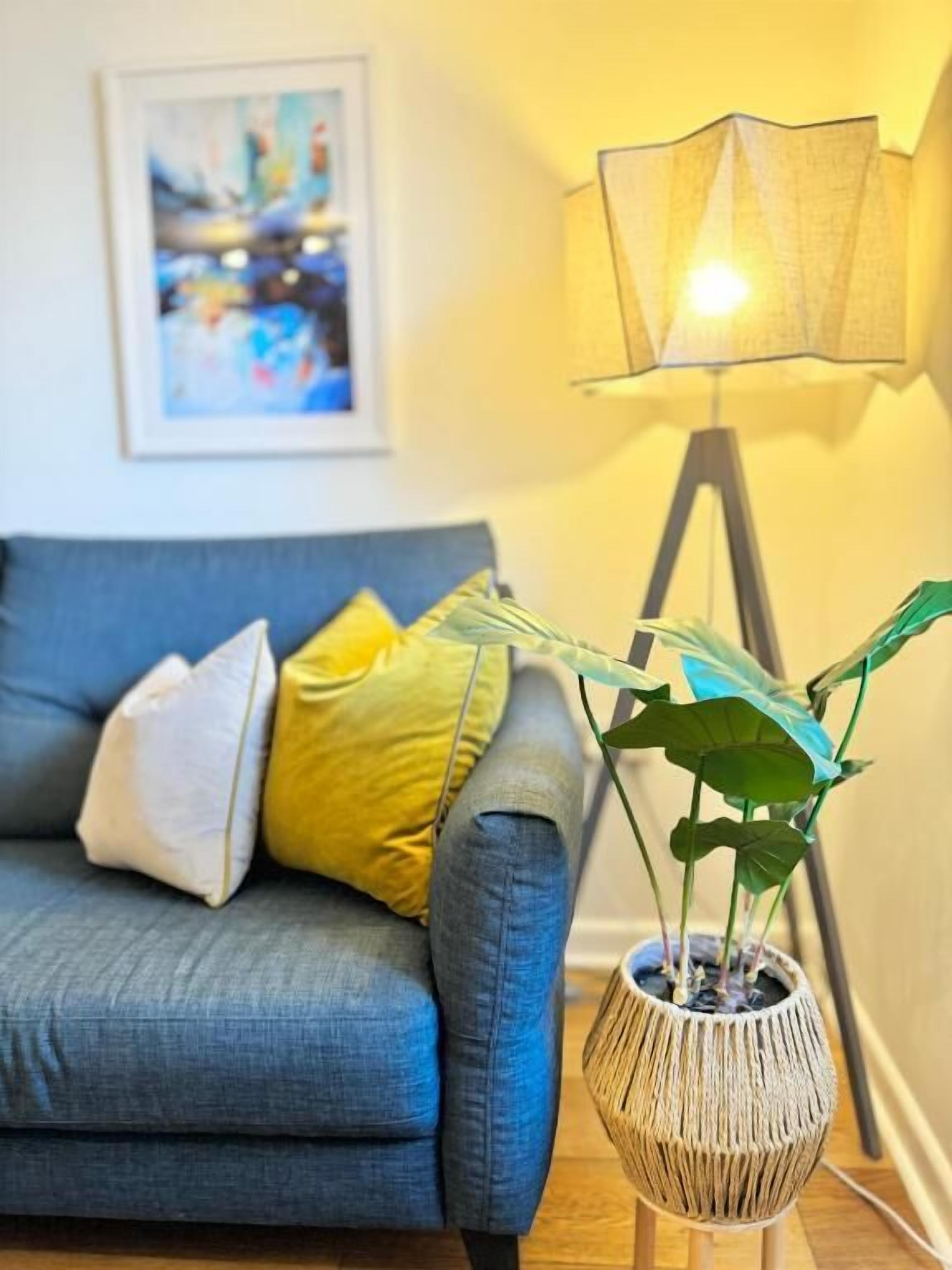 A living room with a blue sofa, a floor lamp, and a potted plant.