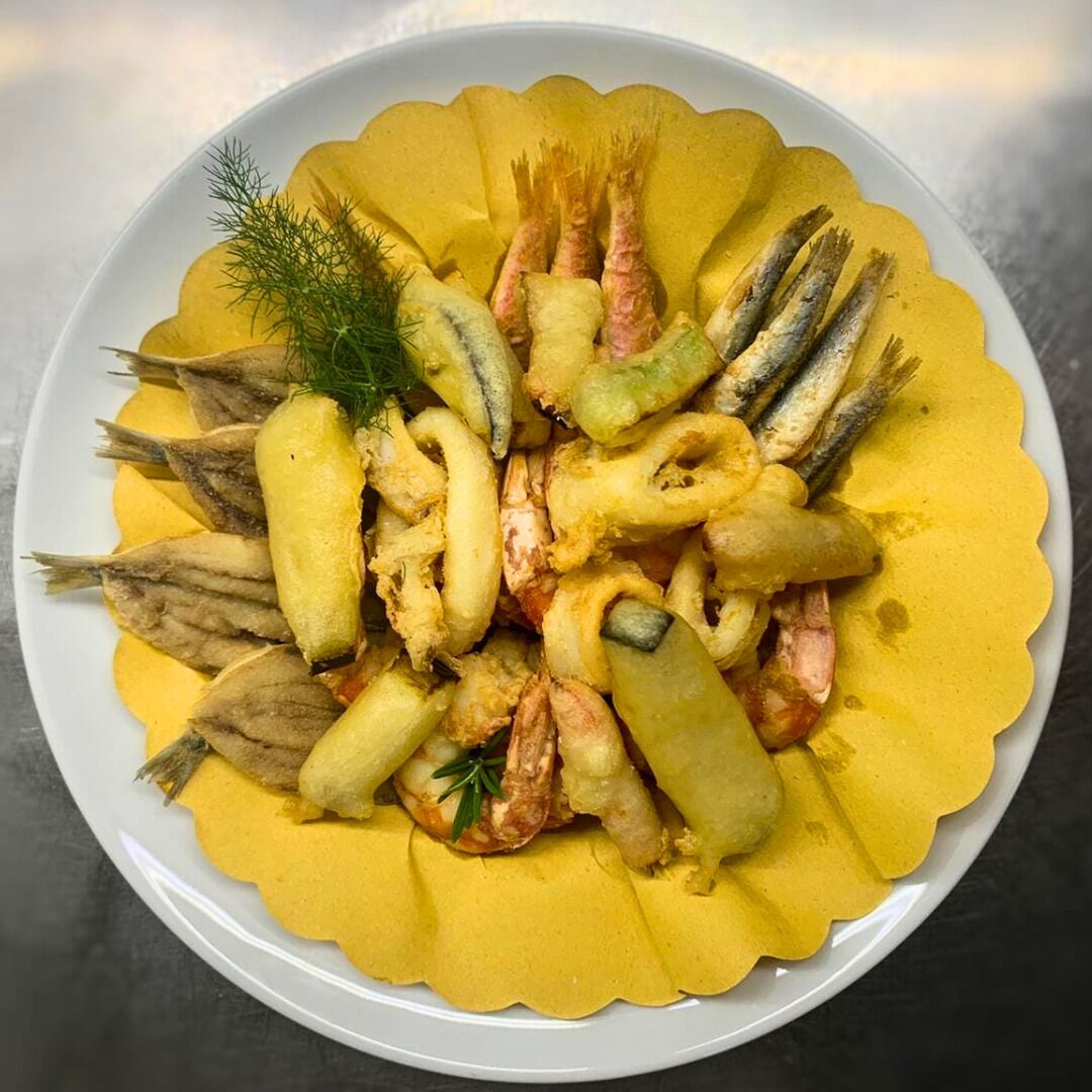 A plate of fried seafood including shrimp, squid, and fish, garnished with dill.
