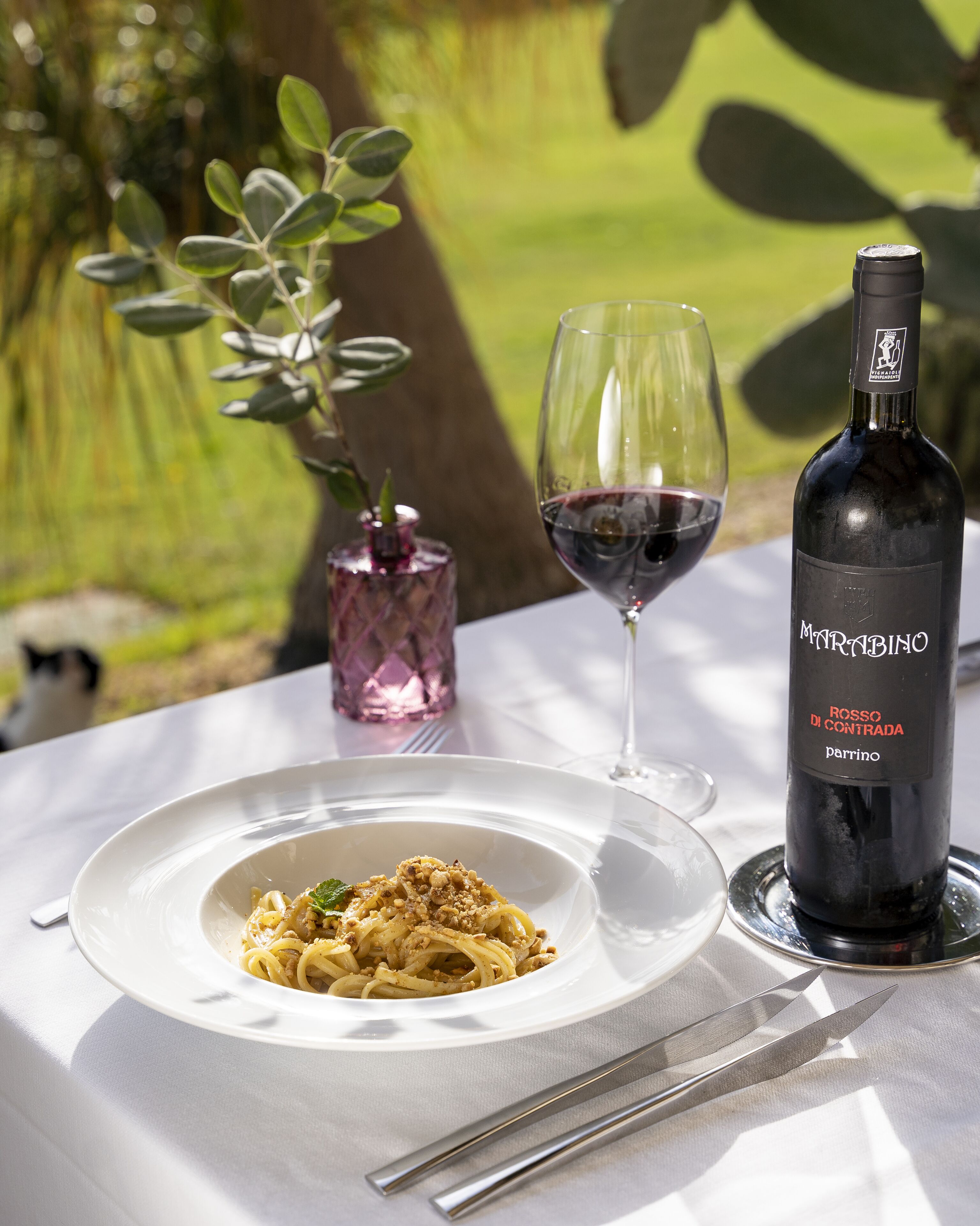 A dining table with a plate of pasta, a wine glass, and a wine bottle.