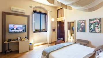 Habitación de hotel con cama, escritorio con televisor, ventana con cortinas y obras de arte en las paredes.
