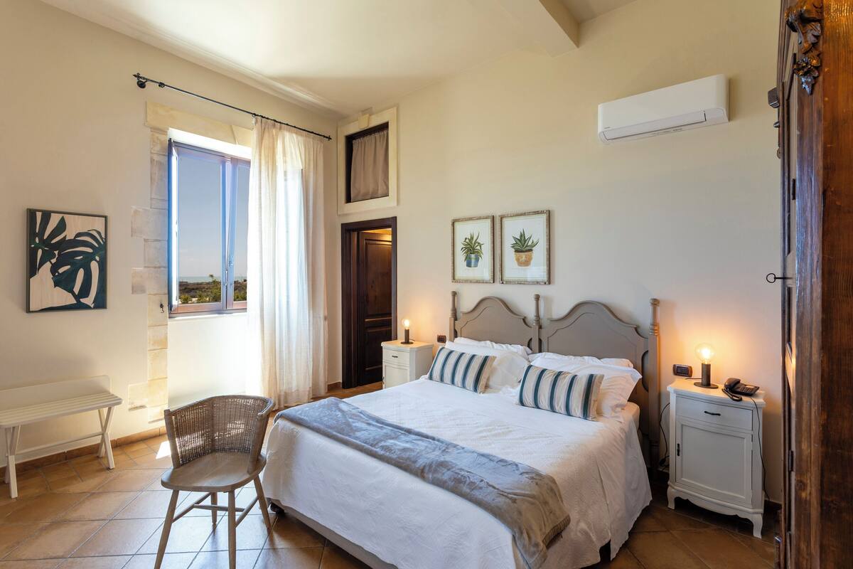 A bedroom with a large bed, bedside tables, a chair, and a window with curtains.