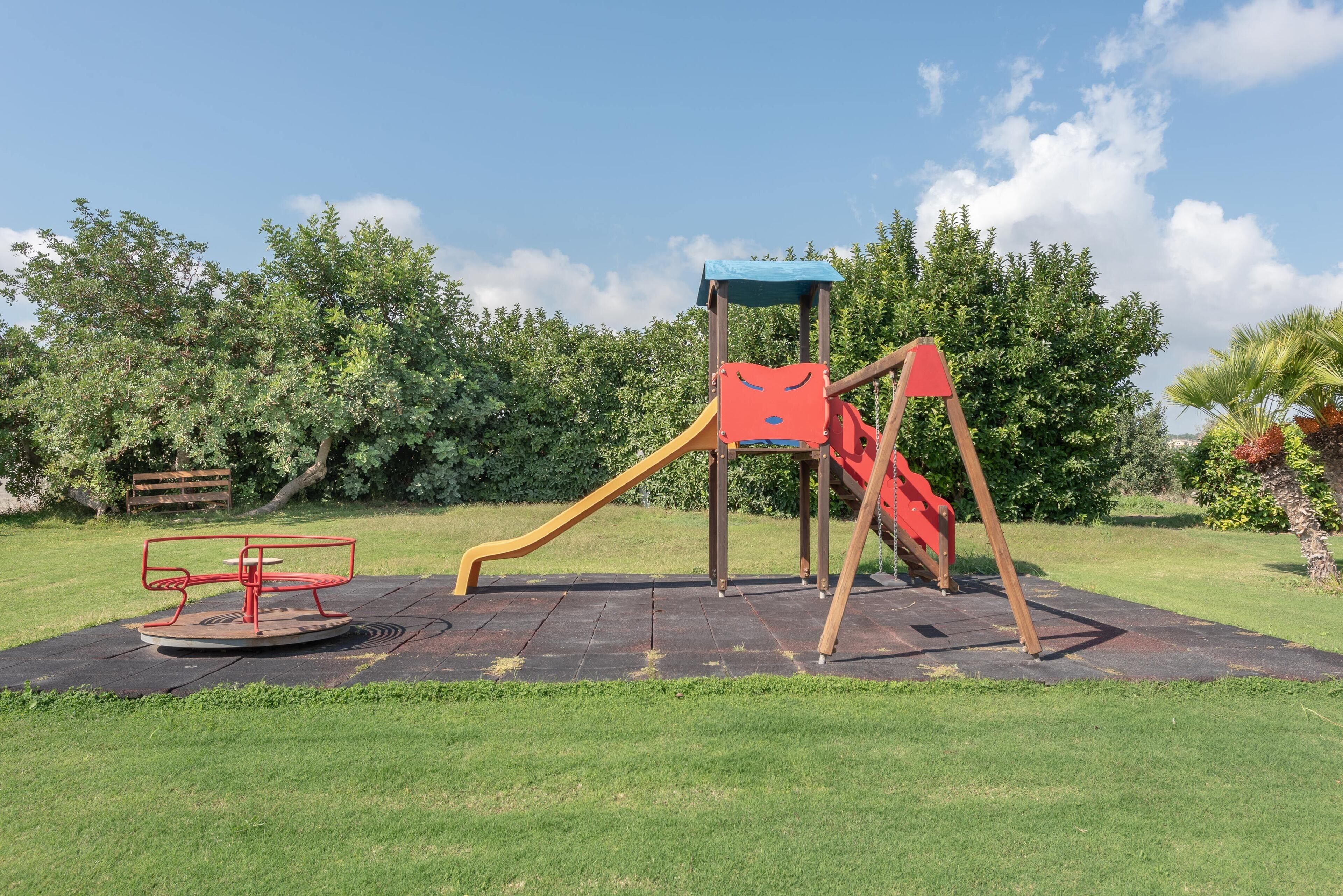 Un parque infantil con tobogán, estructura para escalar y un carrusel.