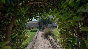 A stone pathway leading to a building with a tiled roof, surrounded by greenery. - Relais Torre Marabino (Ispica)