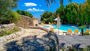 A stone pathway leading to a pool area with lounge chairs and umbrellas. - Relais Torre Marabino (Ispica)