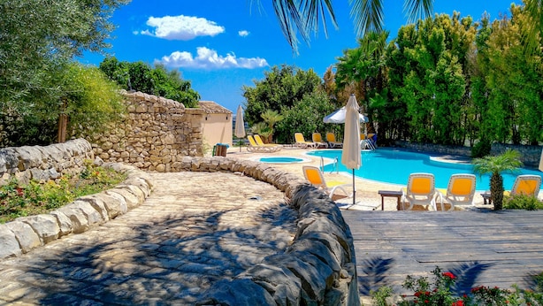 A stone pathway leading to a pool area with lounge chairs and umbrellas. - Relais Torre Marabino (Ispica)