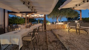 An outdoor dining area with tables and chairs, stone flooring, and a pergola structure. - Relais Torre Marabino (Ispica)