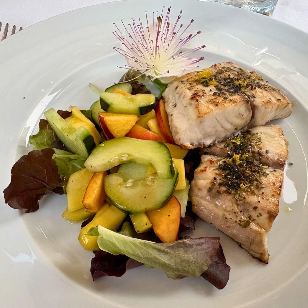 Een bord met gegrilde vis en een salade van gemengde groenten.