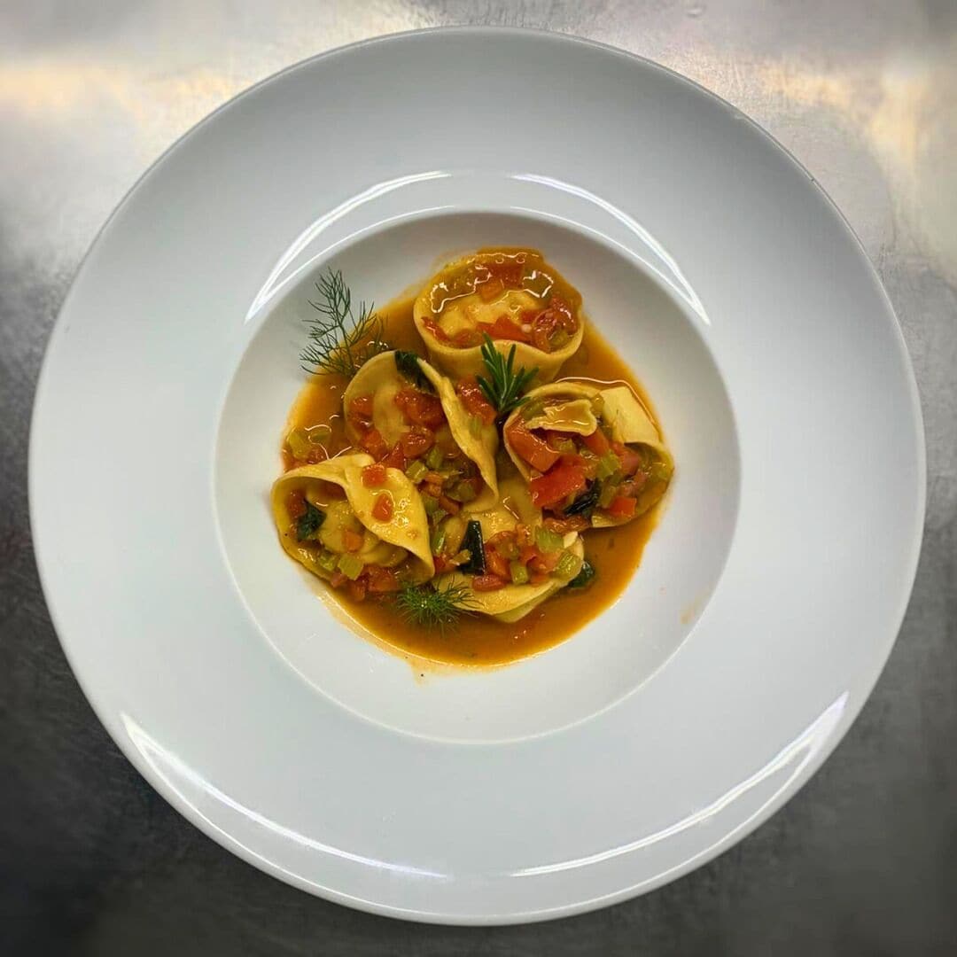 Un plato blanco con ravioles en salsa de tomate, adornado con eneldo.