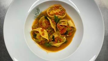 Un plato blanco con ravioles en salsa de tomate, adornado con eneldo.