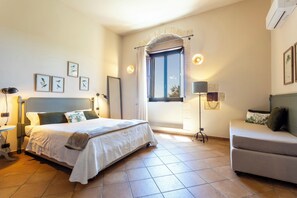 A bedroom with a bed, a sofa, a window with curtains, and wall-mounted lights. - Relais Torre Marabino (Ispica)
