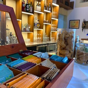 A wooden box with colorful folders, a glass jar with a textured substance, and shelves with bottles and glasses in the background. - Relais Torre Marabino (Ispica)