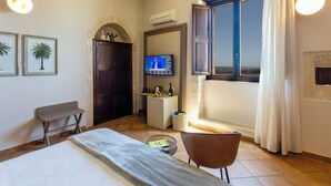 A hotel room with a bed, a desk, a chair, a TV, and a window with curtains. - Relais Torre Marabino (Ispica)