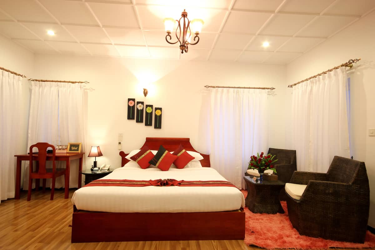 A hotel room with a large bed, a desk with a chair, a small table with a lamp, and a chair.
