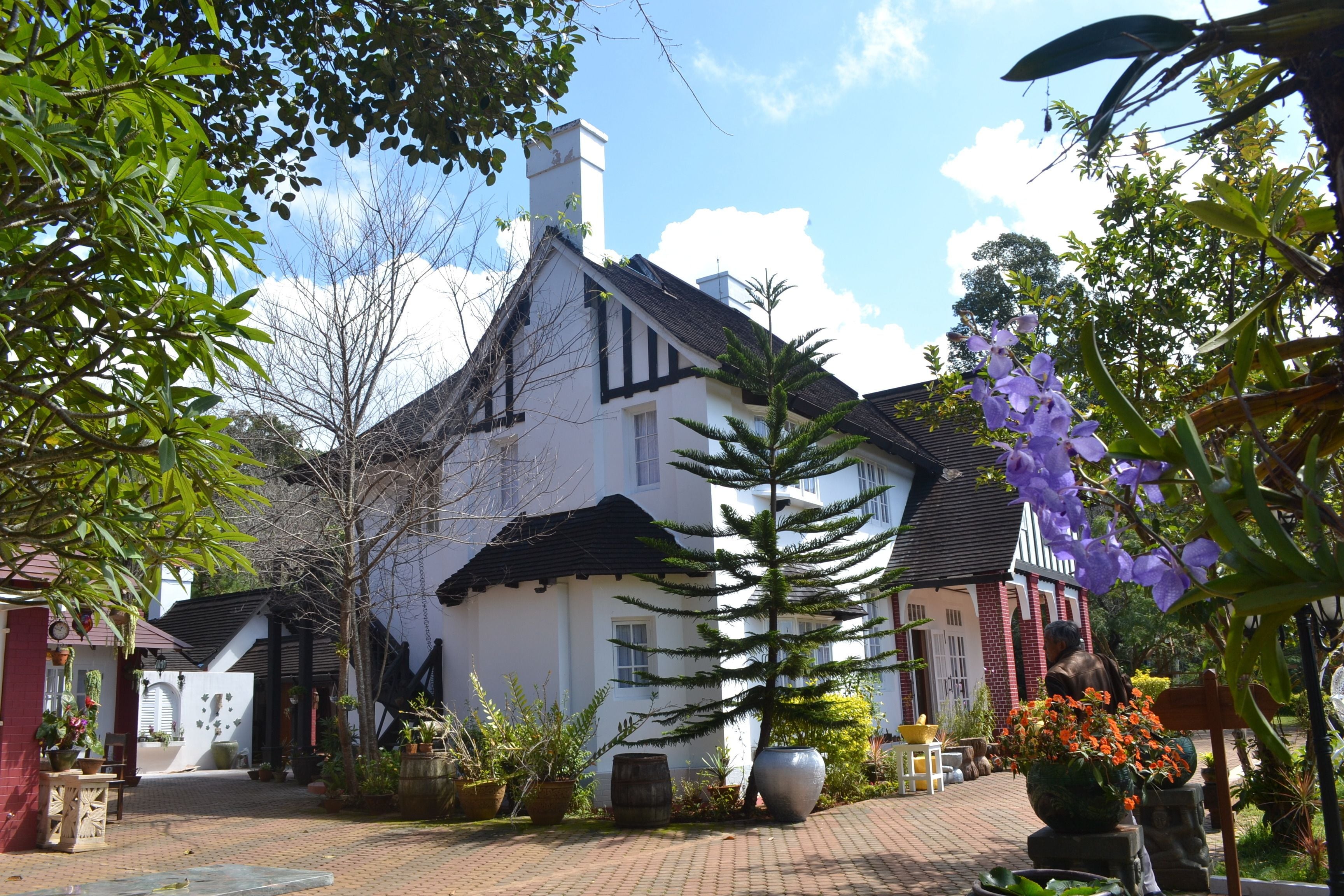 Un bâtiment traditionnel avec une façade en briques, un toit en tuiles et un jardin agrémenté de plantes et de fleurs en pot.