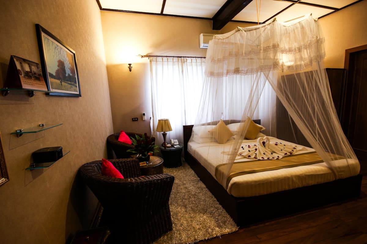 A bedroom with a bed, a chair, a nightstand, a lamp, and a picture on the wall.