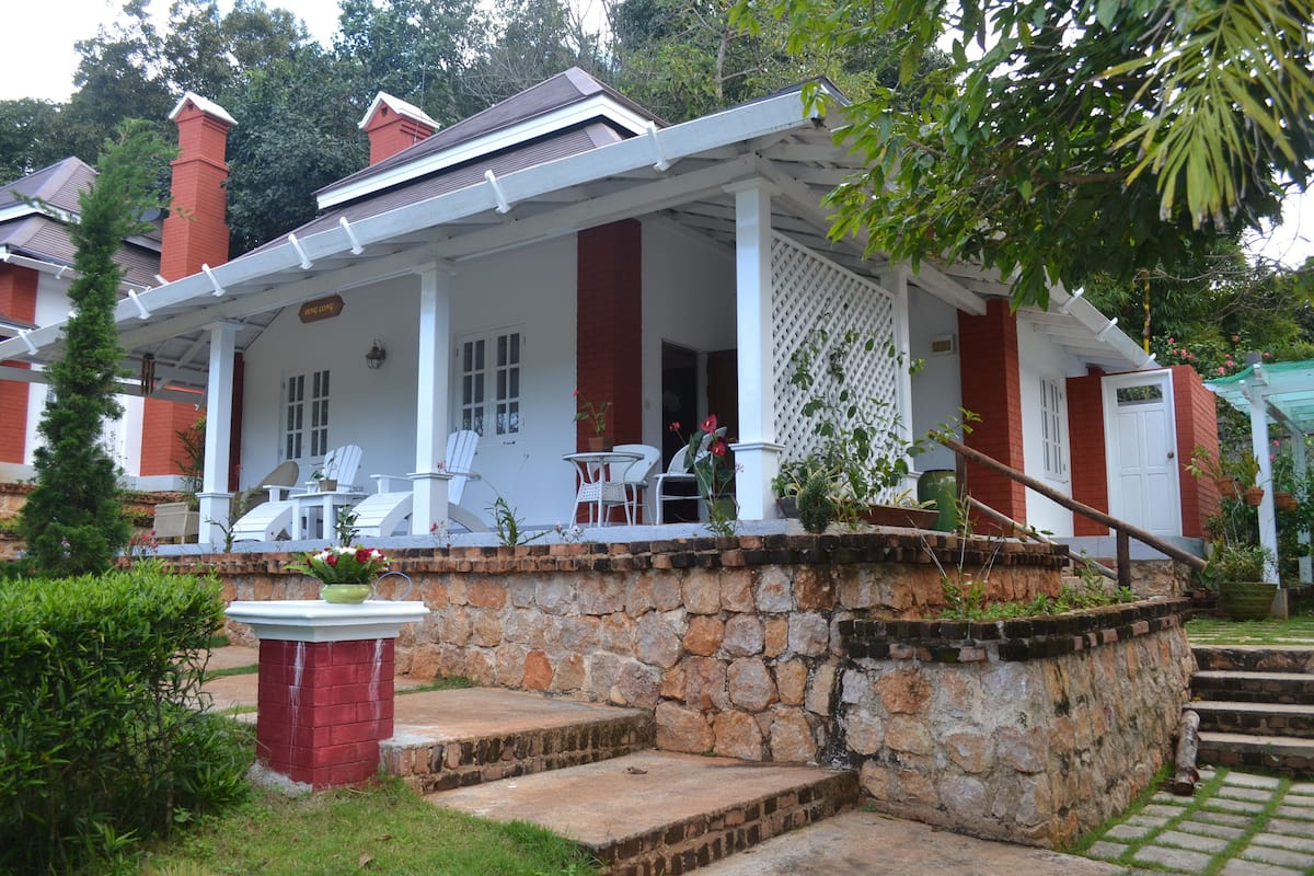 A house with a stone foundation, a porch with white columns, and a red brick chimney.