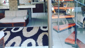 A modern interior with a sofa, a patterned rug, a brick wall, and a staircase visible through a glass door. - Tsumeb Backpackers & Safari (Tsumeb)